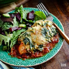 a green plate topped with lasagna covered in sauce next to a salad and fork