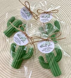 three green cactus shaped cookies wrapped in cellophane and tied with twine on top of a plate