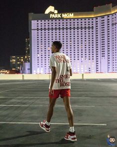 a man walking across an empty parking lot in front of a tall building at night