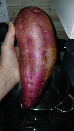 a person holding up a purple potato in front of a stove top oven with the peel still on it's side