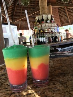 two glasses filled with colored liquid sitting on top of a counter next to a bar