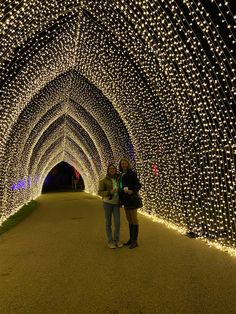 two people standing in front of a tunnel covered with lights