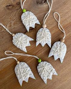 four white and green leaf ornaments hanging from string on a wooden table with wood beads