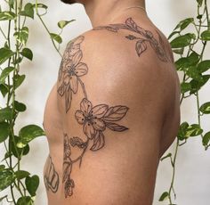 the back of a man's shoulder with flowers and leaves tattooed on his arm