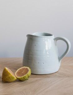 a small white pitcher sitting on top of a wooden table next to a sliced orange