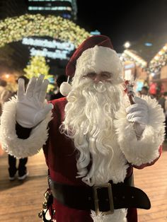 a man dressed as santa clause holding a pipe and wearing white gloves with lights in the background