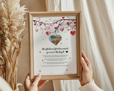 a person holding up a framed poster with hearts and flowers on it, in front of a white curtain