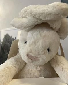 a white stuffed rabbit sitting on top of a table next to a box with its eyes closed