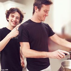 two people standing in front of a stove cooking food on top of a frying pan