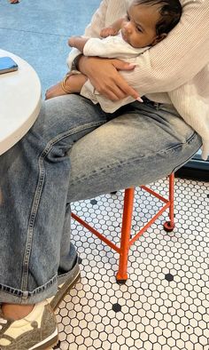 a woman sitting on a stool holding a baby