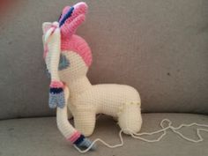 a crocheted pony sitting on top of a couch next to a white cord