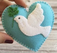 a hand holding a heart shaped ornament with a white dove on it