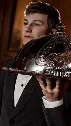 a man in a tuxedo holding a silver platter with an intricate design on it