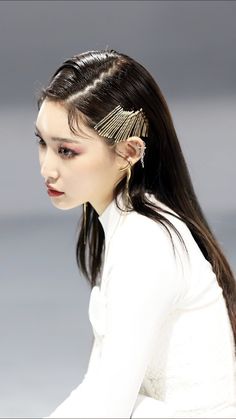 a woman with long black hair and gold ear pins on her head, sitting down