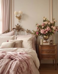 a bed with pink comforter and pillows in a bedroom next to a nightstand with flowers on it