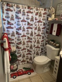 a bathroom decorated for christmas with red trucks on the shower curtain and white tile flooring