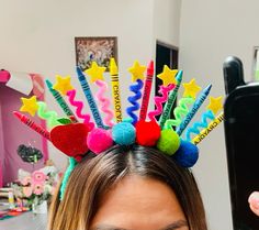 a woman wearing a colorful headpiece with stars and pencils on it's hair