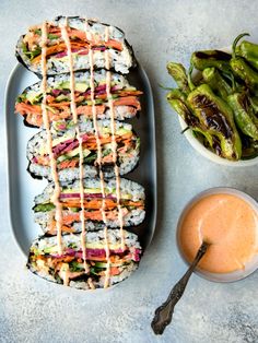 sushi and dipping sauces on a plate next to a bowl of green beans