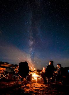 three people sitting around a campfire under the night sky