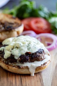 two hamburgers with meat and cheese are on a wooden cutting board next to vegetables