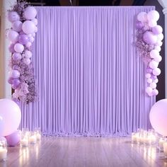 a purple and white backdrop with balloons, candles and flowers on the floor in front of it