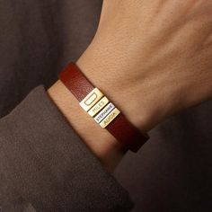 a man wearing a red leather bracelet with two gold bars on it's wrist