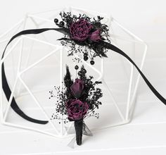 two purple flowers with black ribbons tied around them on a white surface, in front of a geometric structure