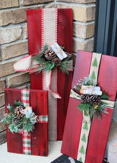 three wrapped presents sitting on the ground next to a brick wall with pine cones and evergreens