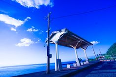 an empty bus stop sitting on the side of a road next to the ocean under a blue sky