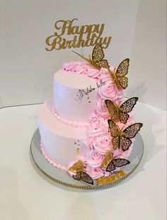 a three tiered cake with pink flowers and butterflies on the top is decorated with gold lettering