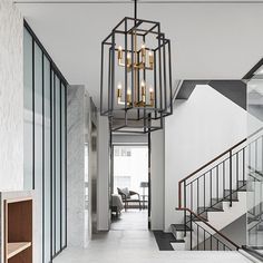 a hallway with stairs and glass doors leading up to the second floor is lit by a chandelier