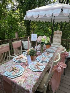 an outdoor table set with pink and white plates, napkins and flowers on it