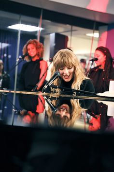 taylor swift singing in front of a microphone with other people behind her at a recording studio