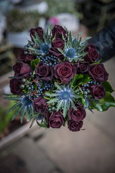 a bouquet of red roses and greenery in someone's hand