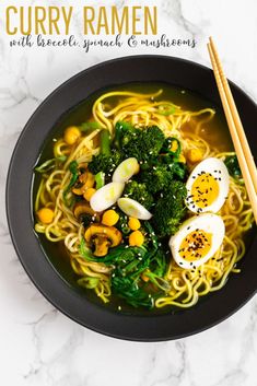 a black bowl filled with noodles, broccoli and hard boiled eggs next to chopsticks