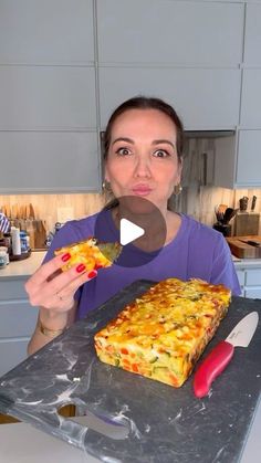 a woman holding up a piece of pizza on top of a counter