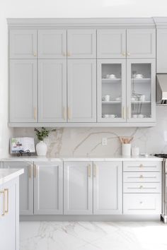 a kitchen with white cabinets and marble counter tops, gold trim on the door handles