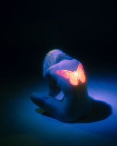 a woman sitting on the ground with her back turned to the camera and glowing in blue light