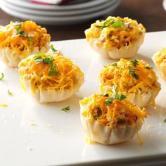 small appetizers with cheese and other toppings sit on a white platter