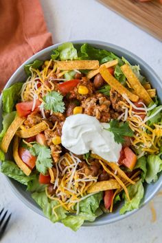 a bowl filled with taco salad on top of a table next to utensils