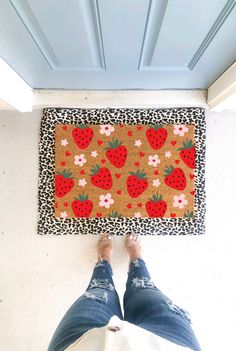 a person standing in front of a door mat with strawberries on it