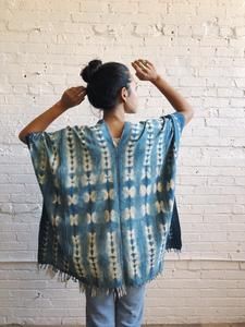 a woman standing in front of a white brick wall wearing a blue and green shawl