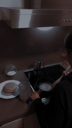 a woman is cooking on the stove in her kitchen with plates and utensils