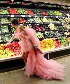 a woman in a pink dress is walking through a produce section