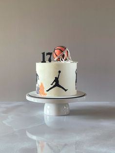 a white cake with black and orange basketballs on it, sitting on a pedestal