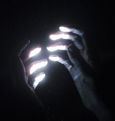 two hands holding something in the dark with light coming from them and one hand reaching for it