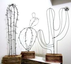 three metal cactus sculptures sitting on top of a table next to a wall with barbed wire