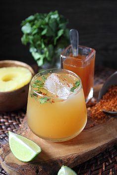 two glasses filled with drinks sitting on top of a wooden table next to limes