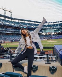 a woman standing on the bleachers at a baseball game with her arms in the air