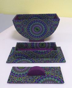 three pieces of art that are sitting on a white table top, one is purple and the other is green